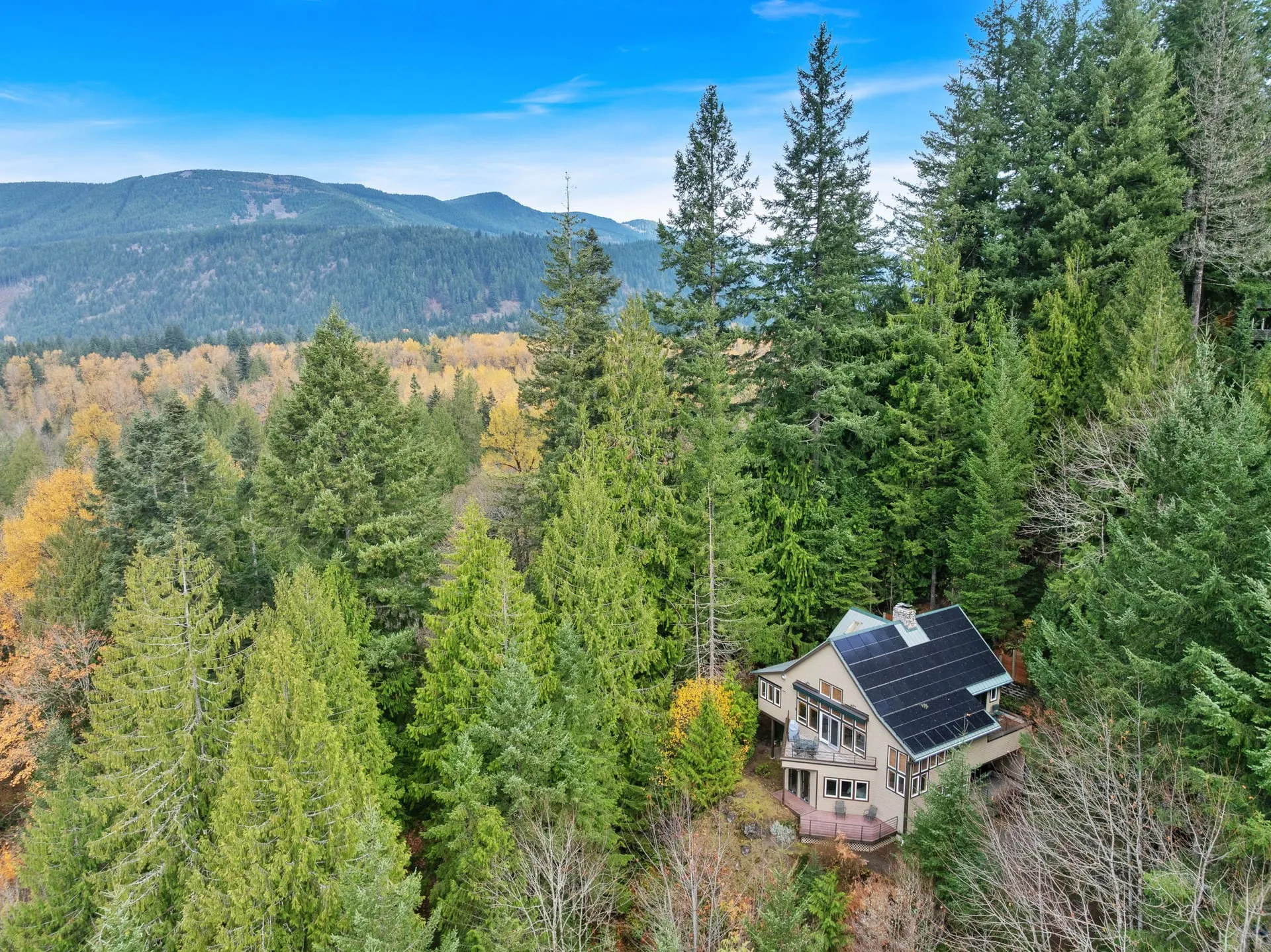 Aerial view of the home on its wooded lot with mountain views